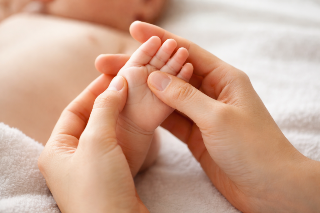 Sanfte Babymassage: Die kleine Hand eines Babys wird behutsam von Erwachsenen Händen massiert.
