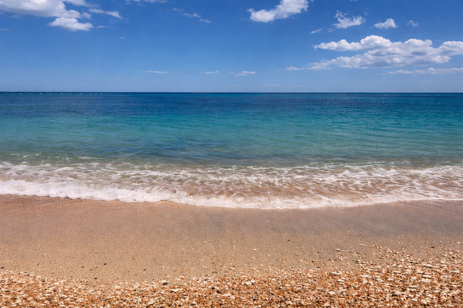 Ruhiger Sandstrand mit Muscheln im Vordergrund, sanften Wellen, türkisblauem Meer und weitem blauen Himmel mit lockeren weißen Wolken im Querformat.